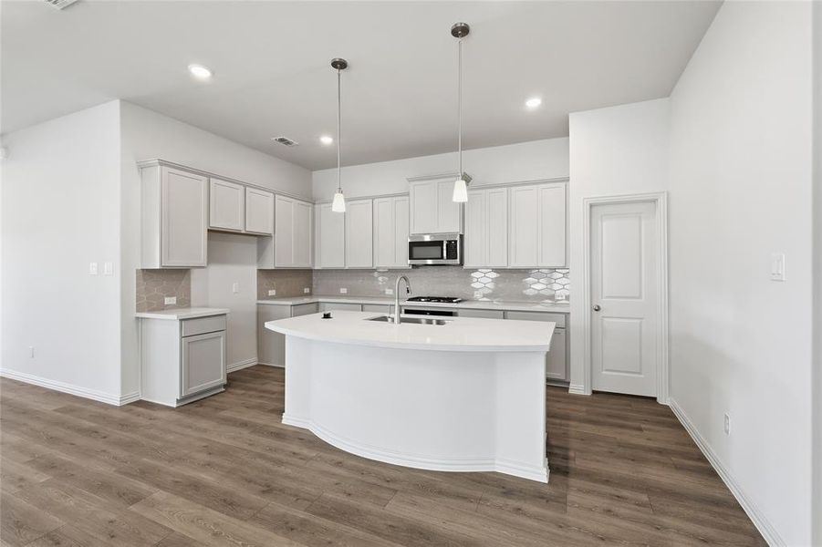 Kitchen with a center island with sink, pendant lighting, stainless steel microwave, and dark wood-type flooring