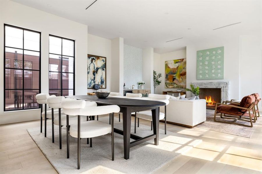 Dining area featuring light wood-style flooring and a warm lit fireplace Dining area featuring light wood-style flooring and a warm lit fireplace
