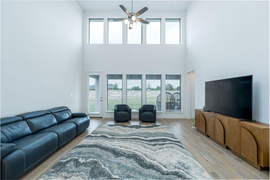 Living room with ceiling fan, healthy amount of natural light, light wood-style flooring, and a high ceiling