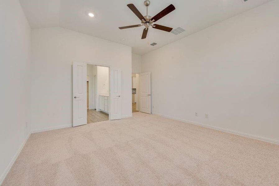 Unfurnished bedroom with light carpet, vaulted ceiling, ensuite bathroom, and ceiling fan