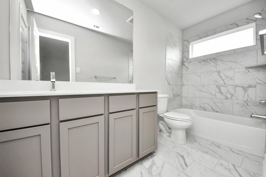 Secondary bath features tile flooring, bath/shower combo with tile surround, light stained wood cabinets, beautiful light countertop.