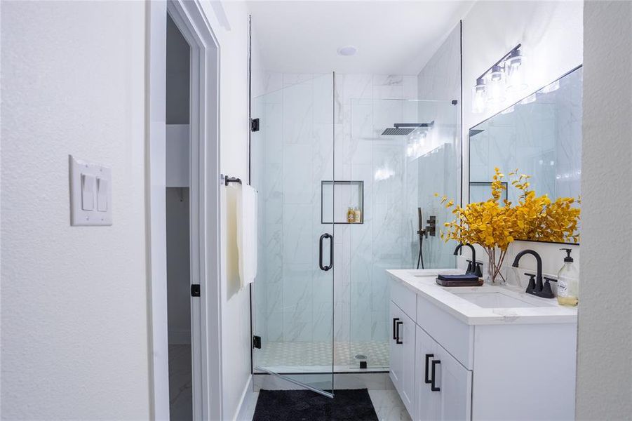Bathroom with double vanity, a marble finish shower, and a textured wall