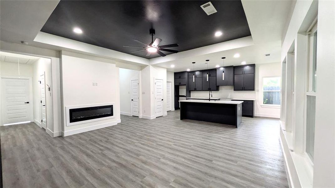 Kitchen with a kitchen island with sink, baseboards, ceiling fan, light countertops, and light wood-style flooring
