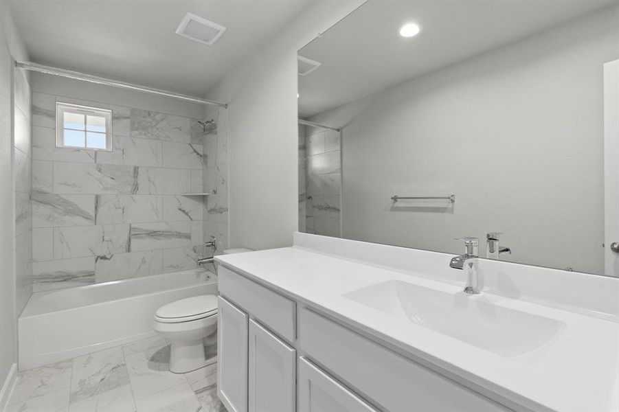 Secondary bath features tile flooring, bath/shower combo with tile surround, light stained wood cabinets, beautiful light countertop. Sample photo of completed home with similar floor plan. As-built interior colors and selections may vary.