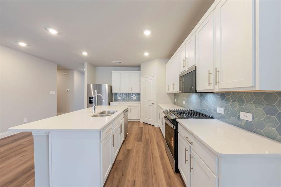 Kitchen with stainless steel appliances, white cabinetry, a kitchen island with sink, decorative backsplash, and light wood-style flooring Kitchen with stainless steel appliances, white cabinetry, a kitchen island with sink, decorative backsplash, and light wood-style flooring