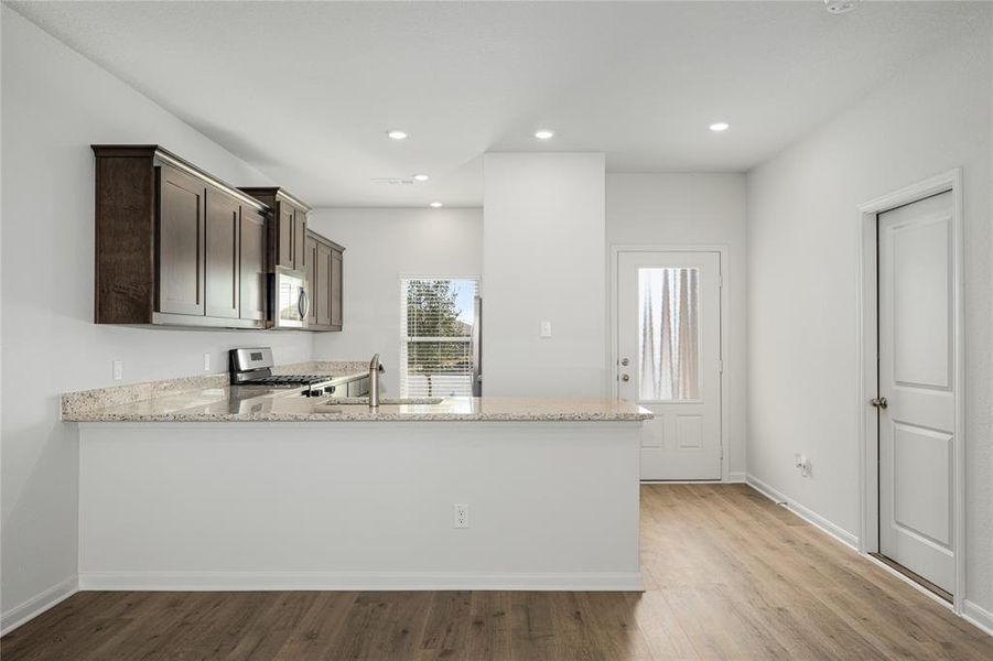 Kitchen with light stone counters, a peninsula, light wood-type flooring, appliances with stainless steel finishes, and recessed lighting
