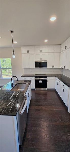 Kitchen featuring hanging light fixtures, stainless steel appliances, dark wood-style floors, white cabinetry, and dark stone countertops Kitchen featuring hanging light fixtures, stainless steel appliances, dark wood-style floors, white cabinetry, and dark stone countertops