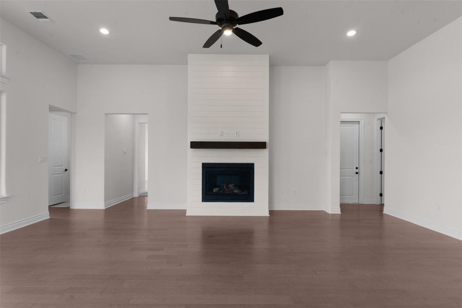 Unfurnished living room featuring a ceiling fan, recessed lighting, dark wood finished floors, a fireplace, and a high ceiling
