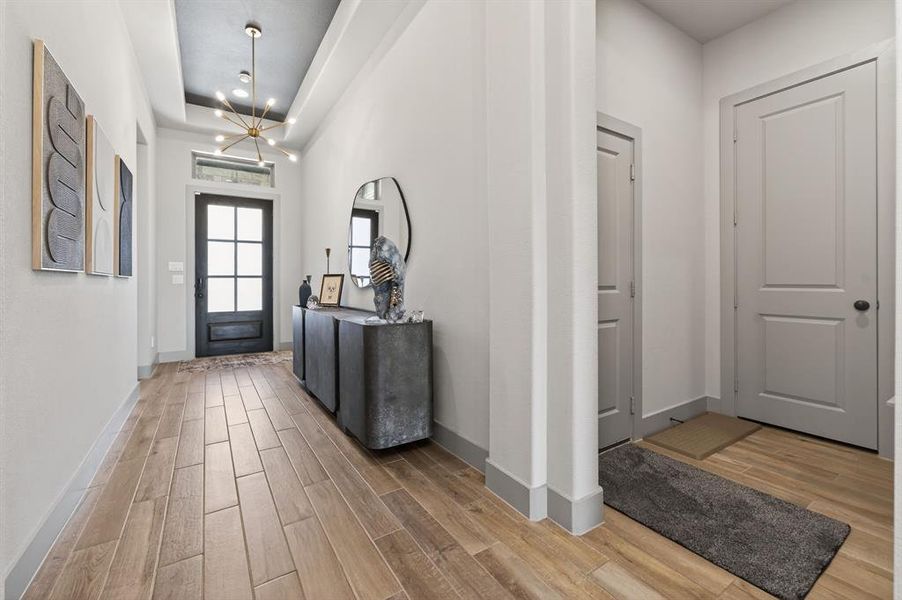 Foyer with light wood finished floors, suspended lighting, and a raised ceiling Foyer with light wood finished floors, suspended lighting, and a raised ceiling