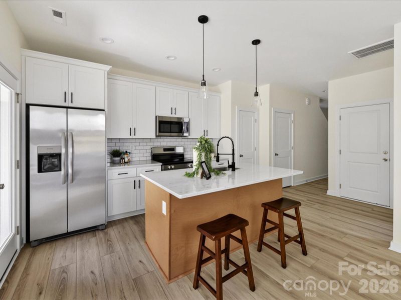 Bright, open-concept kitchen featuring a spacious island with seating, stainless steel appliances, and seamless flow into the sun-filled living area.