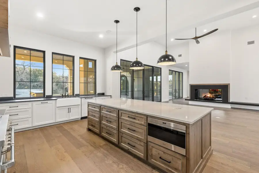 Kitchen with two tone cabinetry, a large island, a multi sided fireplace, stainless steel appliances, and light wood-style floors