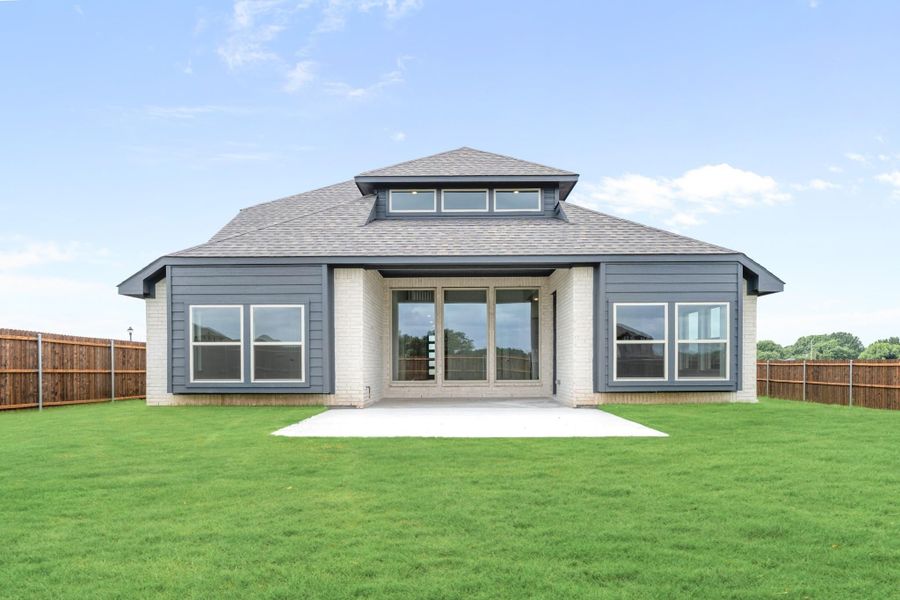 Rear exterior of single-story home with gray siding, brick accents, patio, and fenced backyard Rear exterior of single-story home with gray siding, brick accents, patio, and fenced backyard