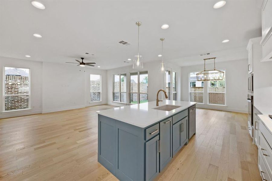 Kitchen island with a light countertop and integrated sink, pendant lighting, hardwood flooring, recessed ceiling lighting, and multiple windows Kitchen island with a light countertop and integrated sink, pendant lighting, hardwood flooring, recessed ceiling lighting, and multiple windows