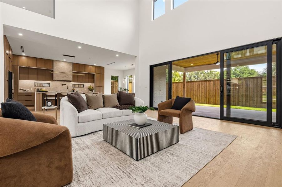 Spacious living area featuring high ceilings, wood-finish flooring, and a modern open-concept kitchen with light wood cabinetry