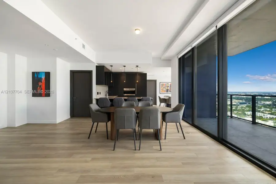 Open-concept floor plan featuring wood-finish flooring, floor-to-ceiling glass sliding doors, a balcony, and built-in cabinetry with integrated appliances