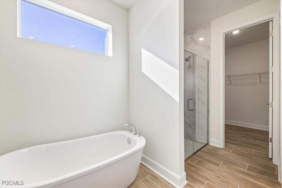 Full bath featuring a marble finish shower, wood finish floors, a freestanding tub, and a spacious closet