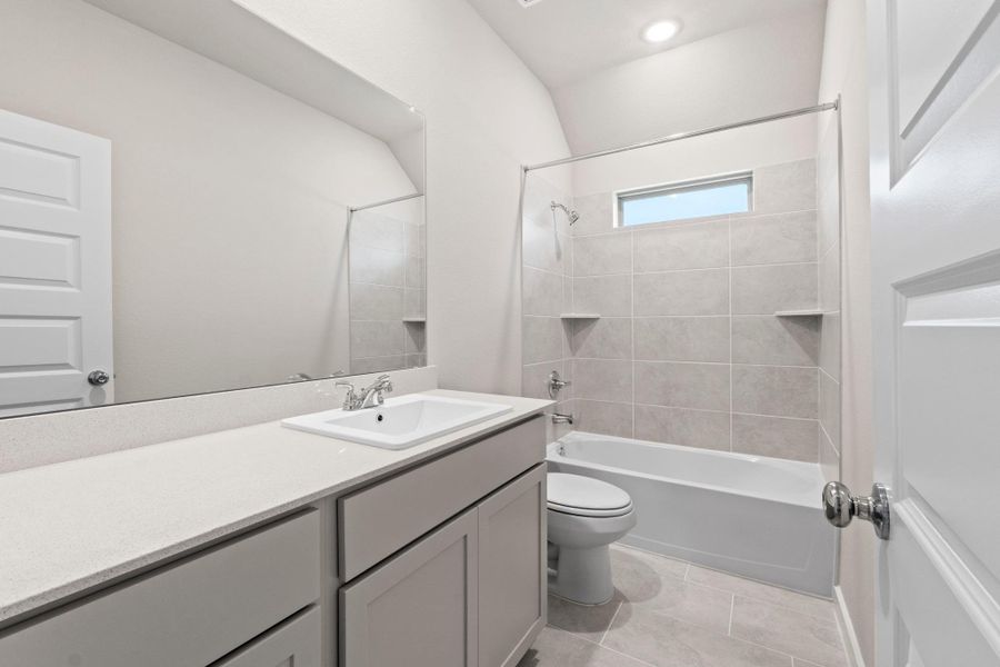 A well-lit bathroom features a single vanity, a standard tub, and neutral tiled flooring.