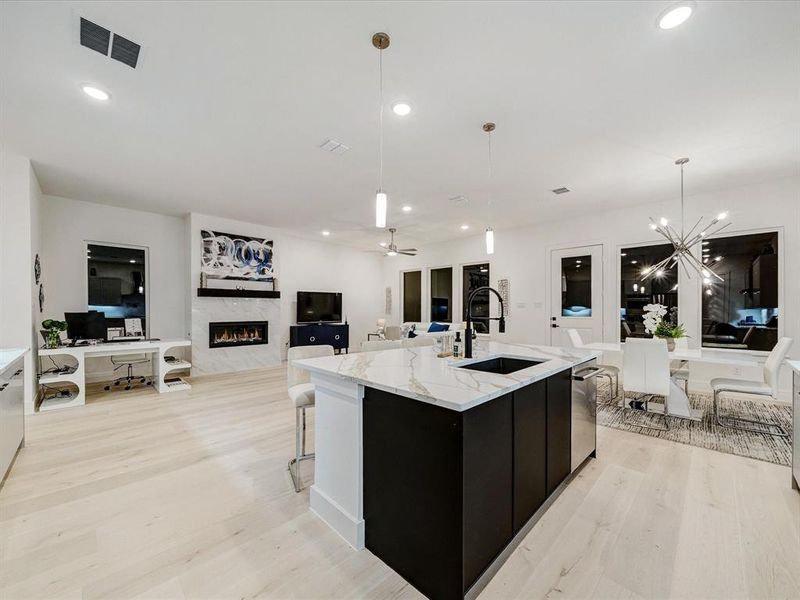 Kitchen featuring pendant lighting, light wood-type flooring, a premium fireplace, open floor plan, and ceiling fan Kitchen featuring pendant lighting, light wood-type flooring, a premium fireplace, open floor plan, and ceiling fan