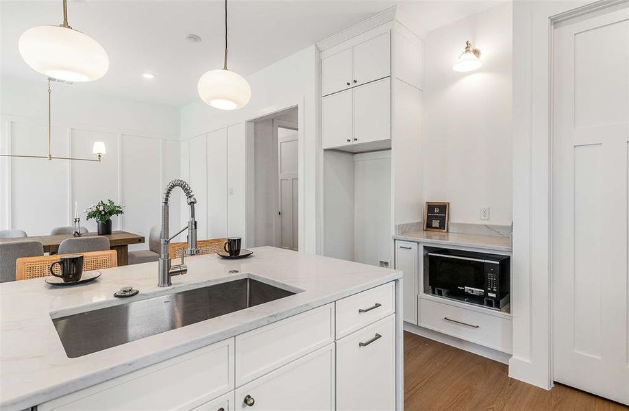 Kitchen featuring white cabinetry, light stone countertops, black microwave, hanging light fixtures, and light wood-type flooring