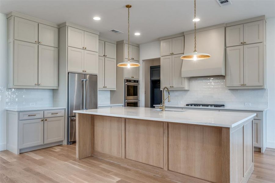 Kitchen with pendant lighting, sink, light hardwood / wood-style flooring, a kitchen island with sink, and stainless steel appliances