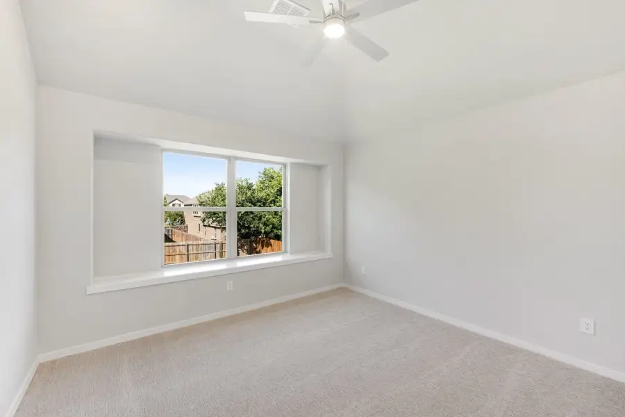 Empty bedroom with carpet flooring, ceiling fan, and large window overlooking backyard