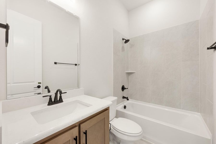 Full bathroom with wood vanity, white quartz countertop, and tiled shower-tub combo with matte black fixtures
