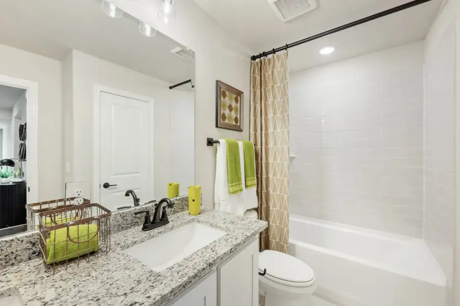 Bathroom with granite countertop vanity, white tub-shower combo, and tiled surround