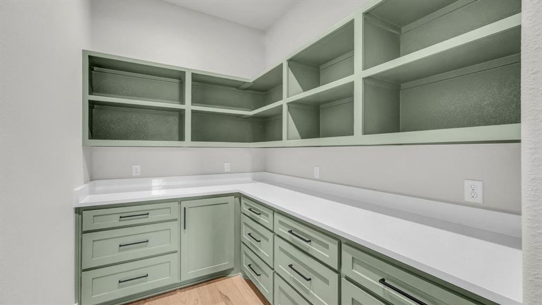Built-in open shelving and lower cabinetry in a light green finish, complemented by a white countertop and wood-finish flooring