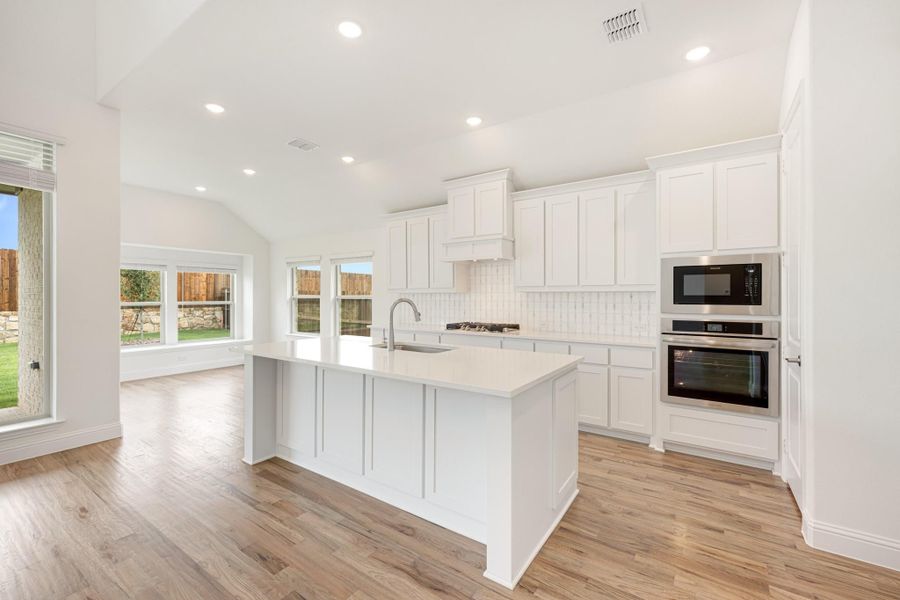 White kitchen with large island, stainless steel double oven, white cabinets, and light hardwood floors White kitchen with large island, stainless steel double oven, white cabinets, and light hardwood floors