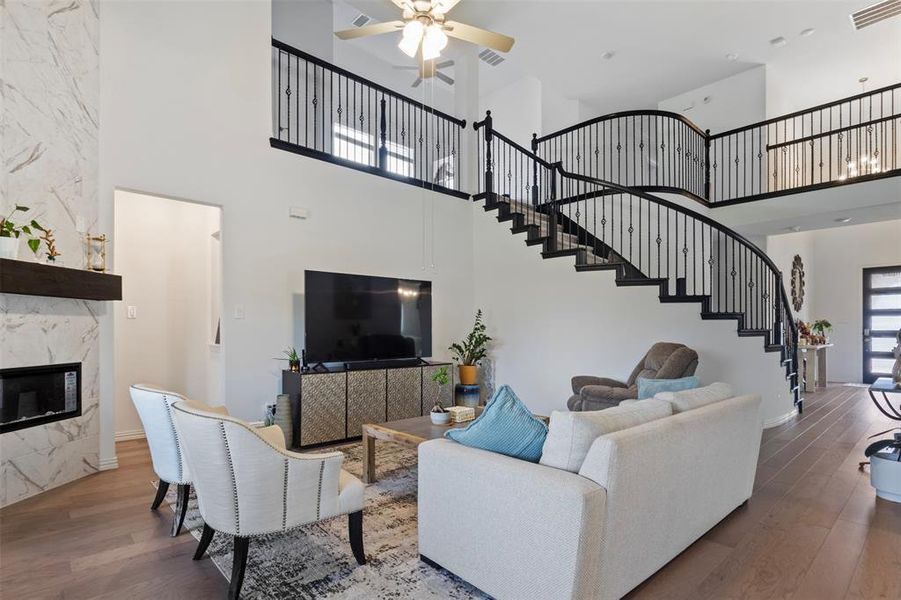 Living area with a towering ceiling, wood finished floors, a premium fireplace, a ceiling fan, and stairway