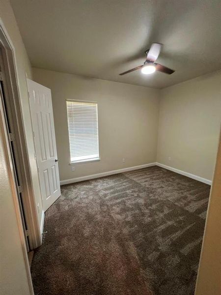 Unfurnished bedroom featuring dark colored carpet and ceiling fan