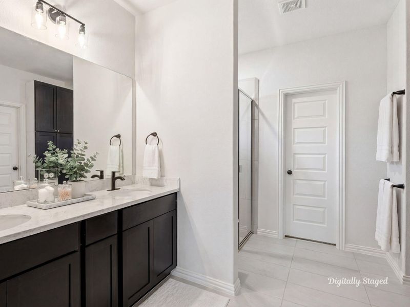 Primary bath offering a dual-sink vanity with stone-look countertops and a large mirror. A built-in linen cabinet, separate glass-enclosed shower, and tile flooring complete this well-appointed space. This photo has been digitally staged to illustrate the possibilities of the home's aesthetic and potential design. Some furnishings and décor shown are for visual inspiration.