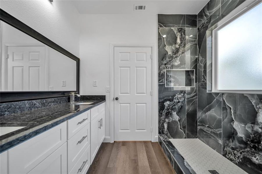 Bathroom featuring a marble finish shower, double vanity, and dark wood-style flooring