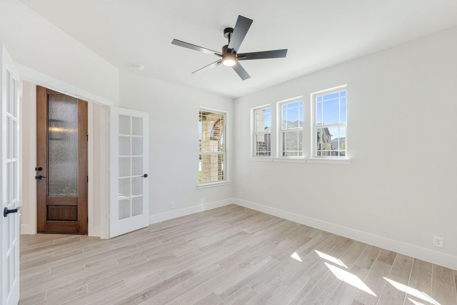 Empty room with light wood-look tile floors, ceiling fan, wood front door, and white French door with multiple windows