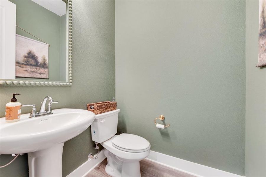 Pedestal sink with chrome faucet, toilet, and wood-finish flooring