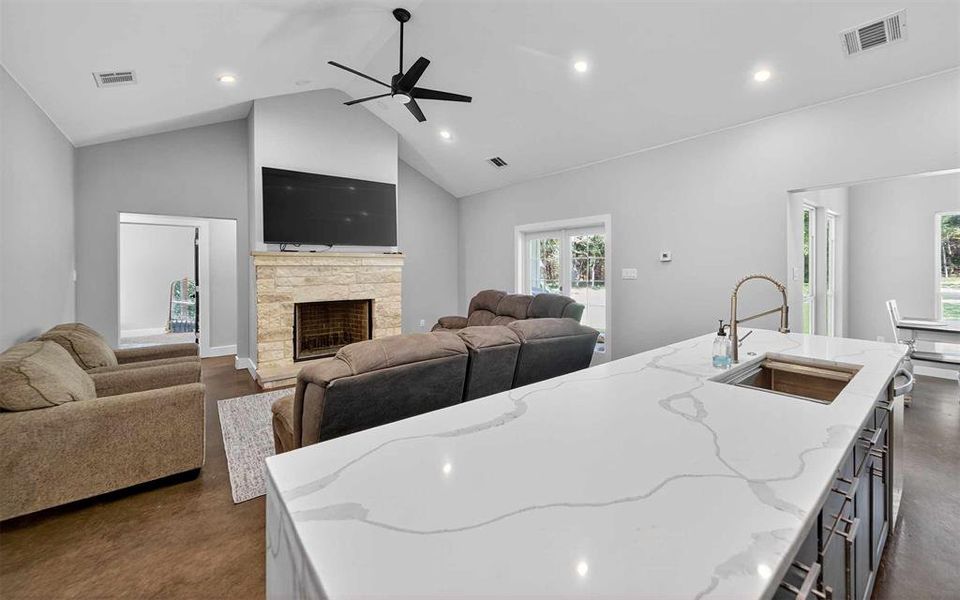 Kitchen with light stone counters, high vaulted ceiling, a center island with sink, a fireplace, and recessed lighting Kitchen with light stone counters, high vaulted ceiling, a center island with sink, a fireplace, and recessed lighting