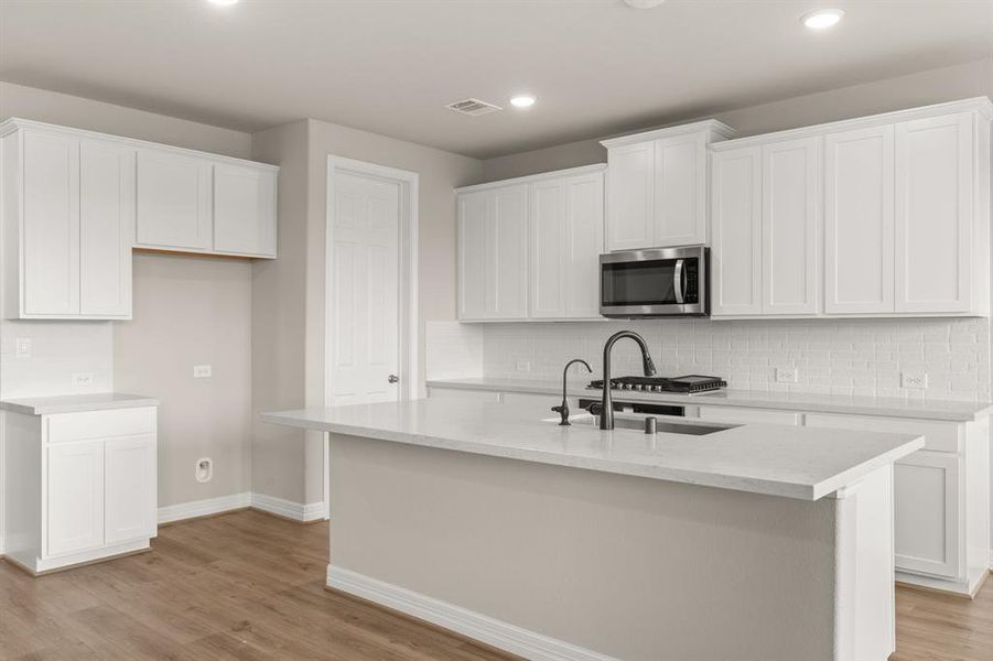 This light and bright kitchen features a large quartz island, white cabinets, a large sink overlooking your family room, recessed lighting, and beautiful backsplash.