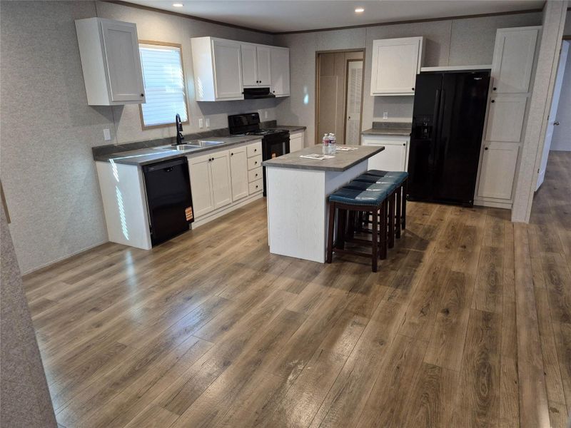 Kitchen featuring black appliances, white cabinetry, a kitchen bar, and recessed lighting