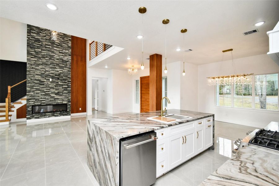 The heart of the home seamlessly connects the gourmet kitchen to a sophisticated living area. Highlights include a contemporary recessed electric fireplace set against a floor-to-ceiling stone accent wall and elegant pendant lighting over the waterfall-edge island.