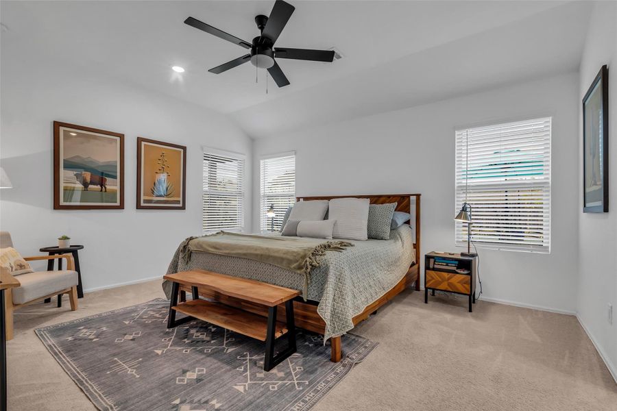 This pictures shows the spacious primary bedroom. Lots of room for furniture and a king size bed. This room consist of 3 large windows, ceiling fan, and neutral carpet.