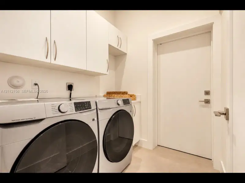 Convenient laundry room with sleek white cabinetry for extra storage and easy-care tile flooring