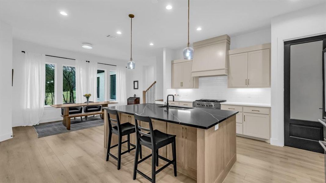 Kitchen featuring a sink, stainless steel range, custom range hood, light wood finished floors, and a breakfast bar area Kitchen featuring a sink, stainless steel range, custom range hood, light wood finished floors, and a breakfast bar area