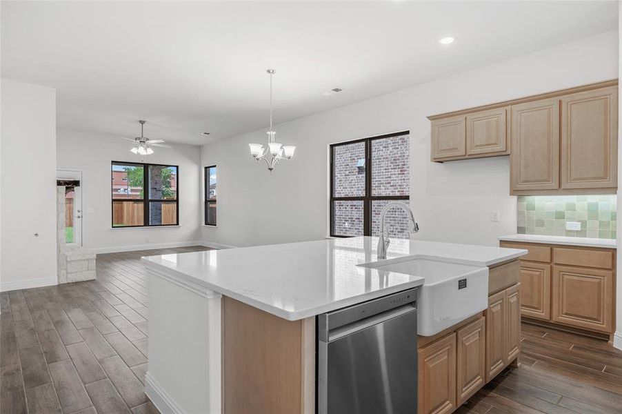 Kitchen with wood finish floors, light brown cabinets, stainless steel dishwasher, backsplash, and a chandelier Kitchen with wood finish floors, light brown cabinets, stainless steel dishwasher, backsplash, and a chandelier