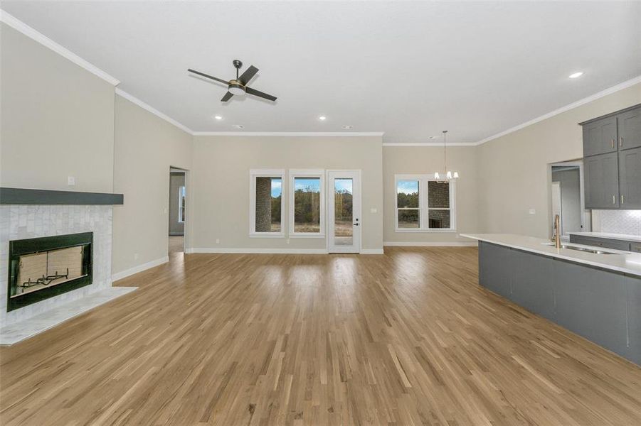 Unfurnished living room featuring sink, light wood-type flooring, crown molding, and a tiled fireplace