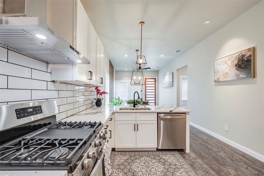 Kitchen featuring stainless steel appliances, wall chimney exhaust hood, white cabinets, a peninsula, and recessed lighting