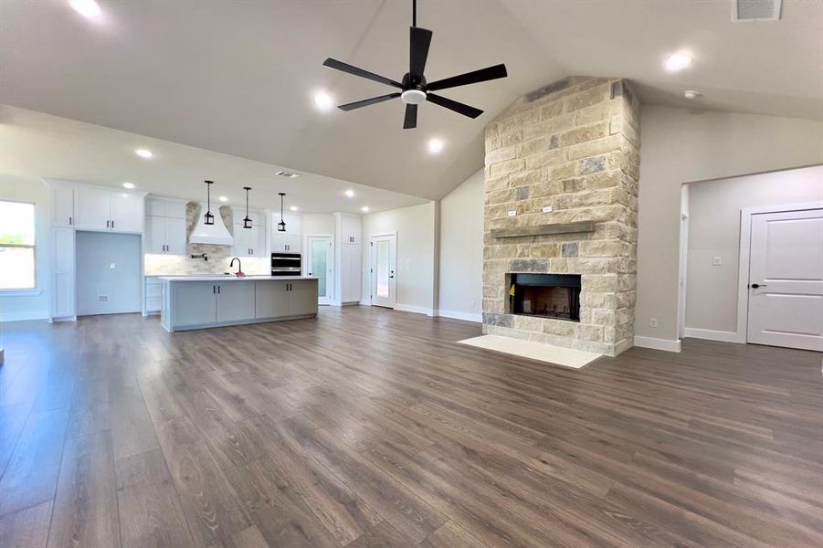 Unfurnished living room with dark finished floors, ceiling fan, a fireplace, high vaulted ceiling, and recessed lighting