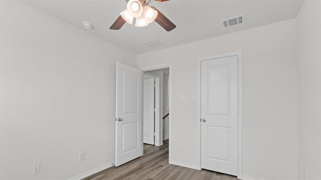 Interior room featuring wood-finish flooring, white walls, and a ceiling fan with integrated lighting Interior room featuring wood-finish flooring, white walls, and a ceiling fan with integrated lighting