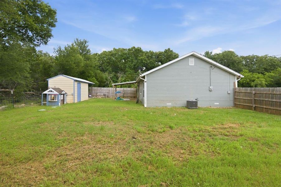 Expansive grassy yard featuring a detached storage shed with a light-colored siding and a wooden privacy fence