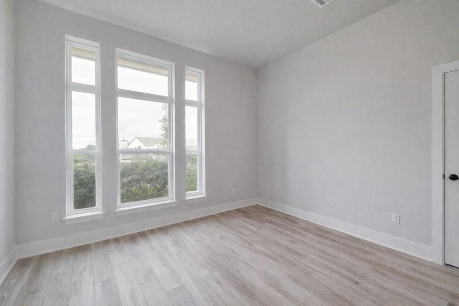 This bright room features light-colored walls and flooring, with three tall windows providing natural light