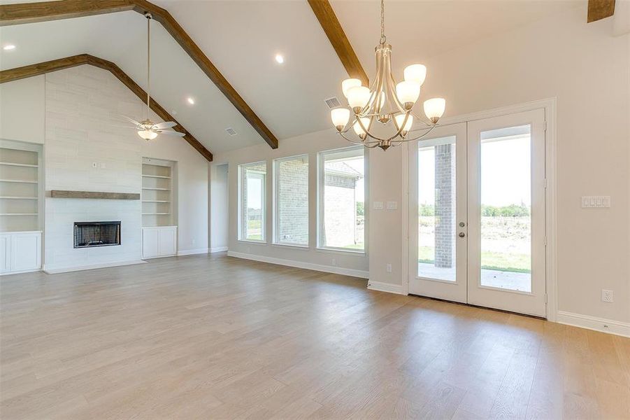 Unfurnished living room featuring a fireplace, light wood-type flooring, built in shelves, beam ceiling, and high vaulted ceiling